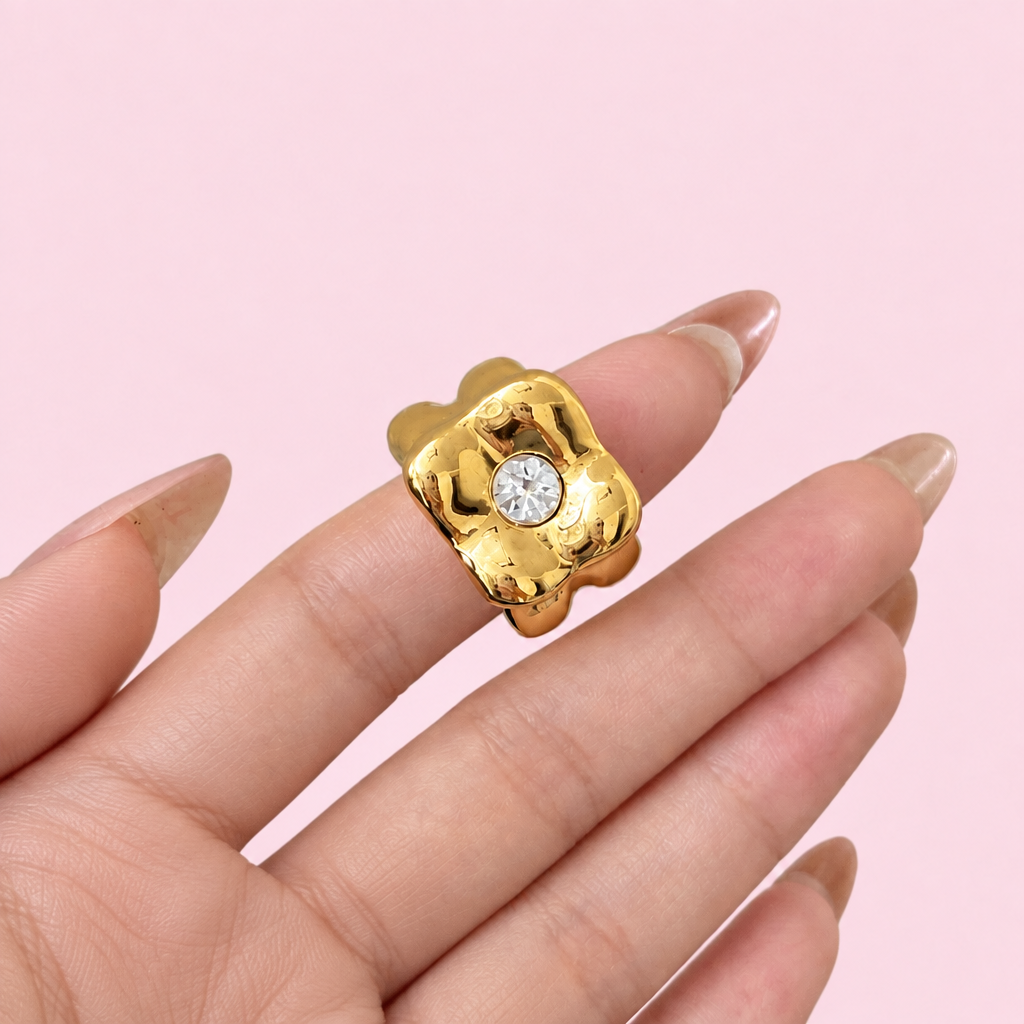 Gold surrealist ring on a hand against a light pink background
